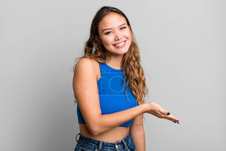 Téléchargez les photos : Jeune jolie femme souriant joyeusement, se sentant heureux et montrant un concept dans l'espace de copie avec la paume de la main - en image libre de droit