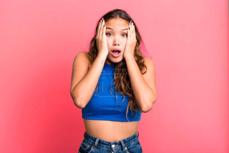 Photo for Young pretty woman looking unpleasantly shocked, scared or worried, mouth wide open and covering both ears with hands - Royalty Free Image