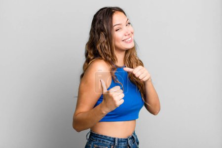 Photo for Young pretty woman smiling cheerfully and casually pointing to copy space on the side, feeling happy and satisfied - Royalty Free Image