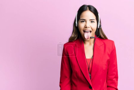 Foto de Hispanic pretty woman with cheerful and rebellious attitude, joking and sticking tongue out. telemarketing concept - Imagen libre de derechos