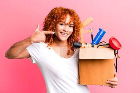 Photo for Red hair pretty woman smiling confidently pointing to own broad smile. housekeeper and toolbox concept - Royalty Free Image