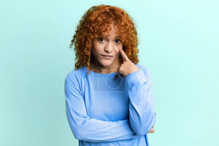Photo for Redhair pretty woman keeping an eye on you, not trusting, watching and staying alert and vigilant - Royalty Free Image