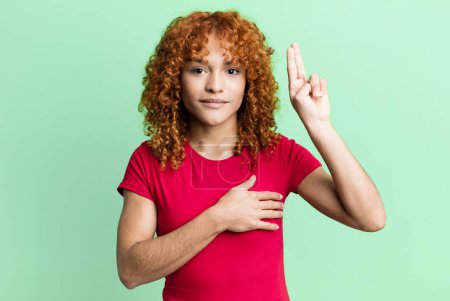 Photo for Redhair pretty woman looking happy, confident and trustworthy, smiling and showing victory sign, with a positive attitude - Royalty Free Image