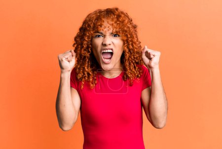 Téléchargez les photos : Redhair pretty woman shouting aggressively with an angry expression or with fists clenched celebrating success - en image libre de droit
