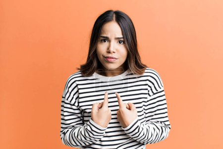 Photo for Hispanic pretty woman pointing to self with a confused and quizzical look, shocked and surprised to be chosen - Royalty Free Image