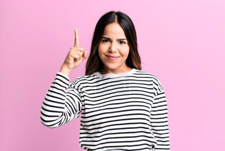 Photo for Hispanic pretty woman feeling like a genius holding finger proudly up in the air after realizing a great idea, saying eureka - Royalty Free Image