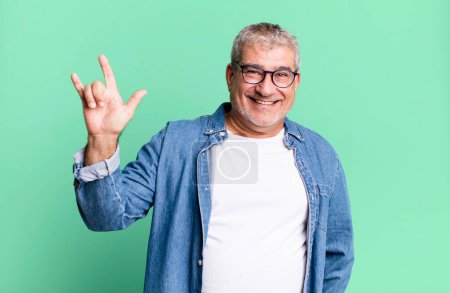 Foto de Hombre mayor de mediana edad sintiéndose feliz, divertido, seguro, positivo y rebelde, haciendo rock o heavy metal signo con la mano - Imagen libre de derechos