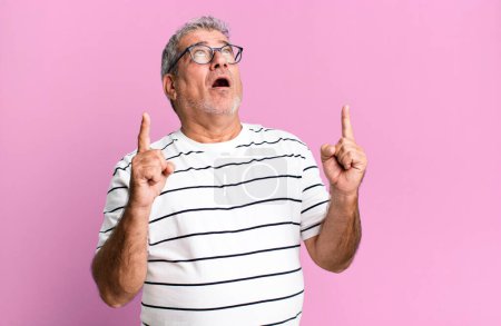 Photo for Middle age senior man looking shocked, amazed and open mouthed, pointing upwards with both hands to copy space - Royalty Free Image