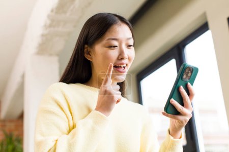 Téléchargez les photos : Asian pretty woman using a smartphone in a cool home - en image libre de droit