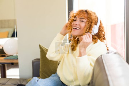 Foto de Young red hair latin pretty woman listening music with headphones at home - Imagen libre de derechos
