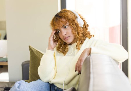 Photo for Young red hair latin pretty woman listening music with headphones at home - Royalty Free Image