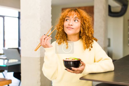 Téléchargez les photos : Jeune roux cheveux latins jolie femme manger ramen nouilles bol à la maison - en image libre de droit