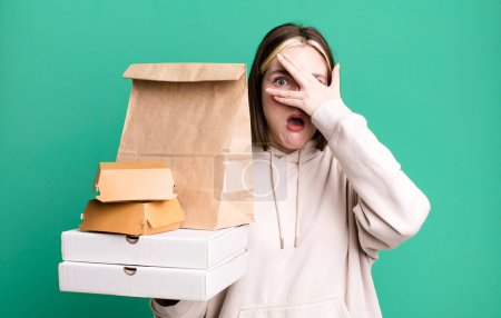 Photo for Young pretty woman looking shocked, scared or terrified, covering face with hand. take away fast food concept - Royalty Free Image