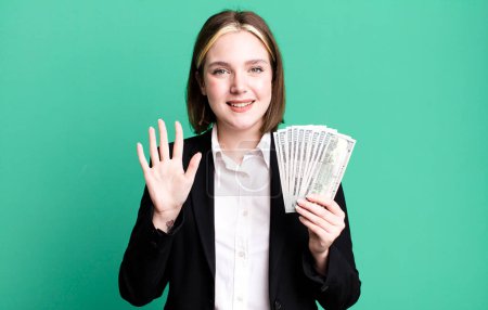 Foto de Young pretty woman smiling and looking friendly, showing number five. dollar banknotes - Imagen libre de derechos