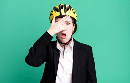 Photo for Young pretty woman looking shocked, scared or terrified, covering face with hand. bike and businesswoman concept - Royalty Free Image