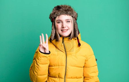 Foto de Young pretty woman smiling and looking friendly, showing number three. cold and coat concept - Imagen libre de derechos