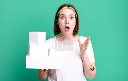 Photo for Young pretty woman amazed, shocked and astonished with an unbelievable surprise. white blank boxes - Royalty Free Image