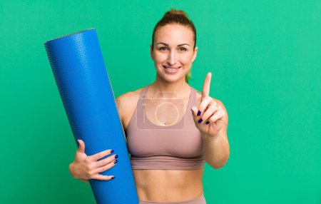 Photo for Young pretty woman smiling and looking friendly, showing number one. fitness and yoga concept - Royalty Free Image