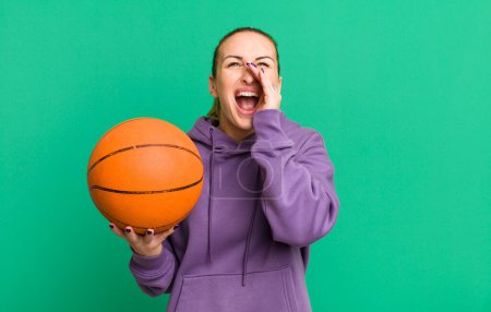 Foto de Young pretty woman feeling happy,giving a big shout out with hands next to mouth. basketball concept - Imagen libre de derechos