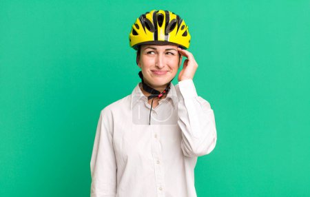 Photo for Young pretty woman smiling happily and daydreaming or doubting. business and bike concept - Royalty Free Image