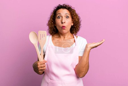 Photo for Pretty middle age woman looking surprised and shocked, with jaw dropped holding an object. home wife chef concept - Royalty Free Image