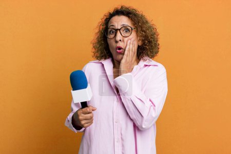 Téléchargez les photos : Pretty middle age woman feeling shocked and scared. tv presenter with a microphone concept - en image libre de droit