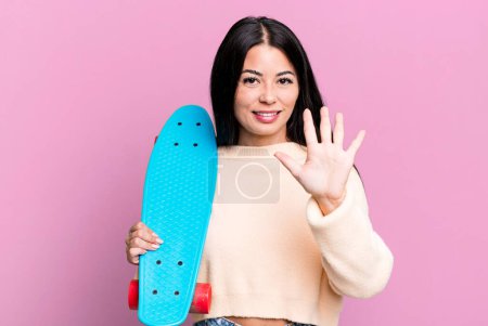 Foto de Hispanic pretty woman smiling and looking friendly, showing number five. skate boarding concept - Imagen libre de derechos