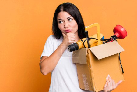 Photo for Hispanic pretty woman thinking, feeling doubtful and confused with a tool box - Royalty Free Image