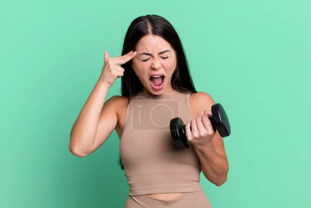 Foto de Hispanic pretty woman looking unhappy and stressed, suicide gesture making gun sign. fitness concept and dumbbell - Imagen libre de derechos