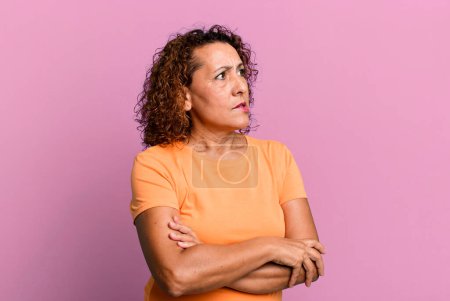 Téléchargez les photos : Femme hispanique d'âge moyen doutant ou pensant, mordant la lèvre et se sentant mal à l'aise et nerveux, cherchant à copier l'espace sur le côté - en image libre de droit