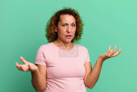 Téléchargez les photos : Middle age hispanic woman shrugging with a dumb, crazy, confused, puzzled expression, feeling annoyed and clueless - en image libre de droit