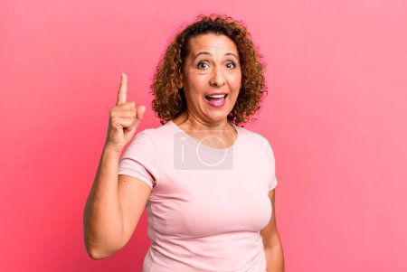 Foto de Mujer hispana de mediana edad sintiéndose como un genio feliz y emocionado después de darse cuenta de una idea, alegremente levantando el dedo, eureka! - Imagen libre de derechos