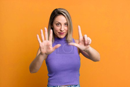 Foto de Rubia mujer adulta sonriendo y buscando amigable, mostrando el número siete o séptimo con la mano hacia adelante, cuenta atrás - Imagen libre de derechos