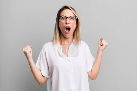 Photo for Blonde adult woman shouting aggressively with an angry expression or with fists clenched celebrating success - Royalty Free Image
