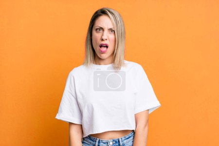 Téléchargez les photos : Blonde adult woman feeling puzzled and confused, with a dumb, stunned expression looking at something unexpected - en image libre de droit