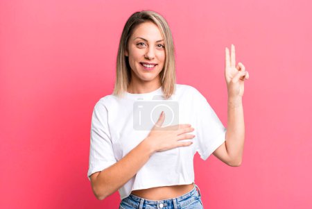 Photo for Blonde adult woman looking happy, confident and trustworthy, smiling and showing victory sign, with a positive attitude - Royalty Free Image