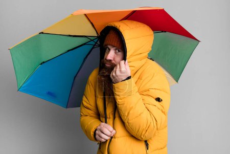 Téléchargez les photos : Longue barbe et cheveux roux homme cool avec parapluie, chapeau et un manteau. concept de motte et d'hiver - en image libre de droit