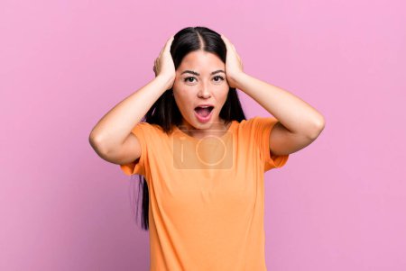 Photo for Pretty latin woman looking unpleasantly shocked, scared or worried, mouth wide open and covering both ears with hands - Royalty Free Image