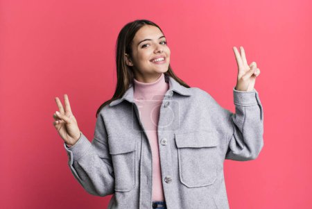 Foto de Pretty young adult woman smiling and looking happy, friendly and satisfied, gesturing victory or peace with both hands - Imagen libre de derechos