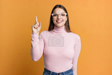 Téléchargez les photos : Jolie jeune femme adulte souriant joyeusement et joyeusement, pointant vers le haut avec une main pour copier l'espace - en image libre de droit