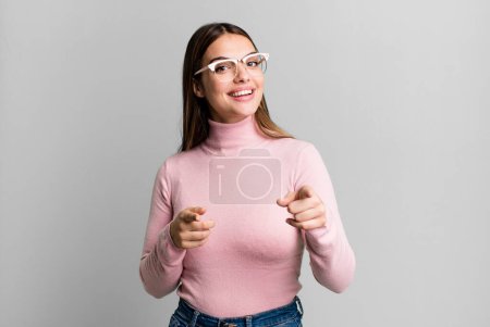 Téléchargez les photos : Pretty young adult woman smiling with a positive, successful, happy attitude pointing to the camera, making gun sign with hands - en image libre de droit