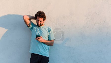 Foto de Joven barbudo hombre usando su teléfono inteligente contra fondo blanco de la pared - Imagen libre de derechos