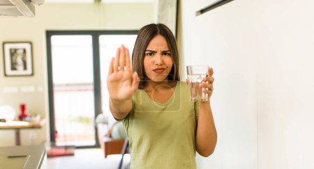 Téléchargez les photos : Jolie femme latine avec un verre d'eau à la maison - en image libre de droit