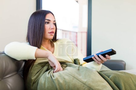 Photo for Young pretty woman watching tv and sitting on a couch at home - Royalty Free Image