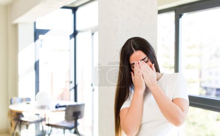 Foto de Young adult pretty woman feeling sad, frustrated, nervous and depressed, covering face with both hands, crying - Imagen libre de derechos