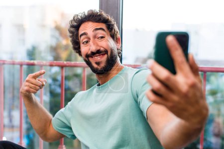 Téléchargez les photos : Jeune homme barbu fou adulte avec un smartphone. vue intérieure - en image libre de droit