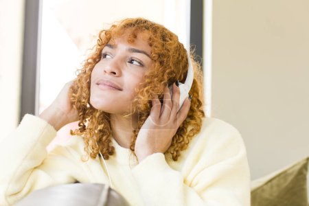 Téléchargez les photos : Young red hair latin pretty woman listening music with headphones at home - en image libre de droit