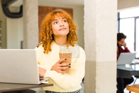 Téléchargez les photos : Jeune roux cheveux latins jolie femme teleconmmuting à la maison avec un ordinateur portable - en image libre de droit