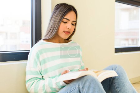 Foto de Bonita mujer latina leyendo un libro en casa - Imagen libre de derechos