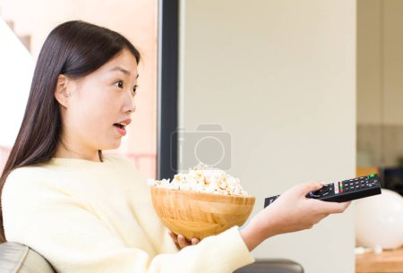 Téléchargez les photos : Asian pretty woman eating popcorns and watching a film at home - en image libre de droit